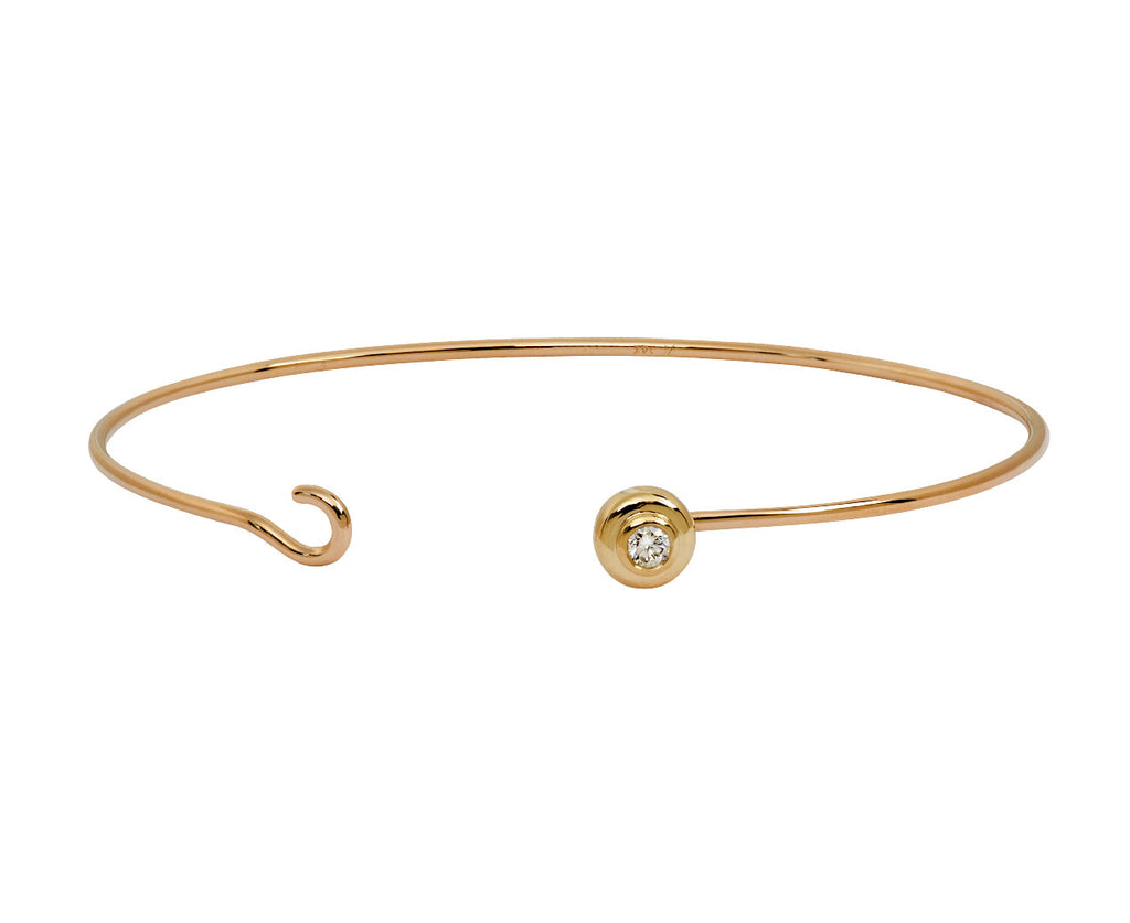 A thin gold open cuff bangle bracelet with a small round bezel-set clear gemstone on one end, shown against a plain white background.